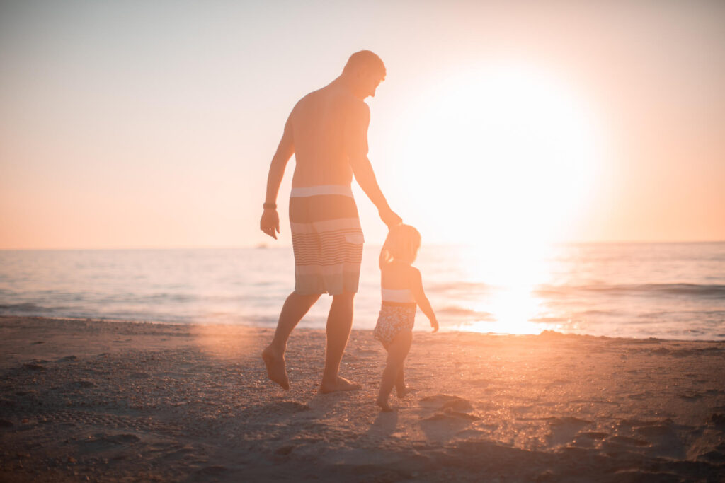 father and child walking on beach near ocean