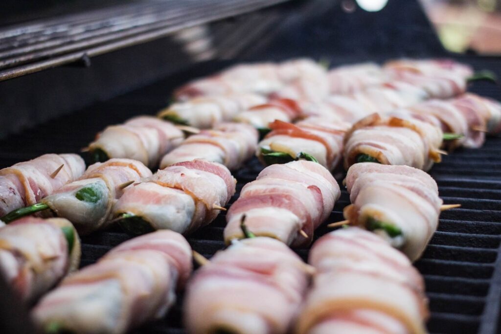 Bacon-wrapped jalapeño poppers grilling on an outdoor grill.