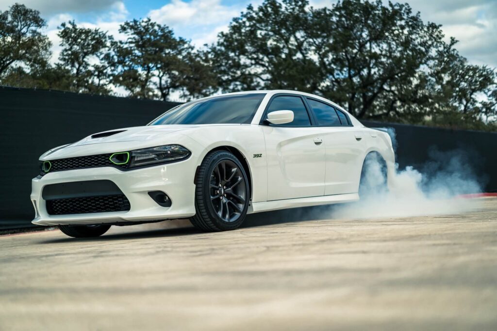 A white Dodge Charger does burnouts in a parking lot. 