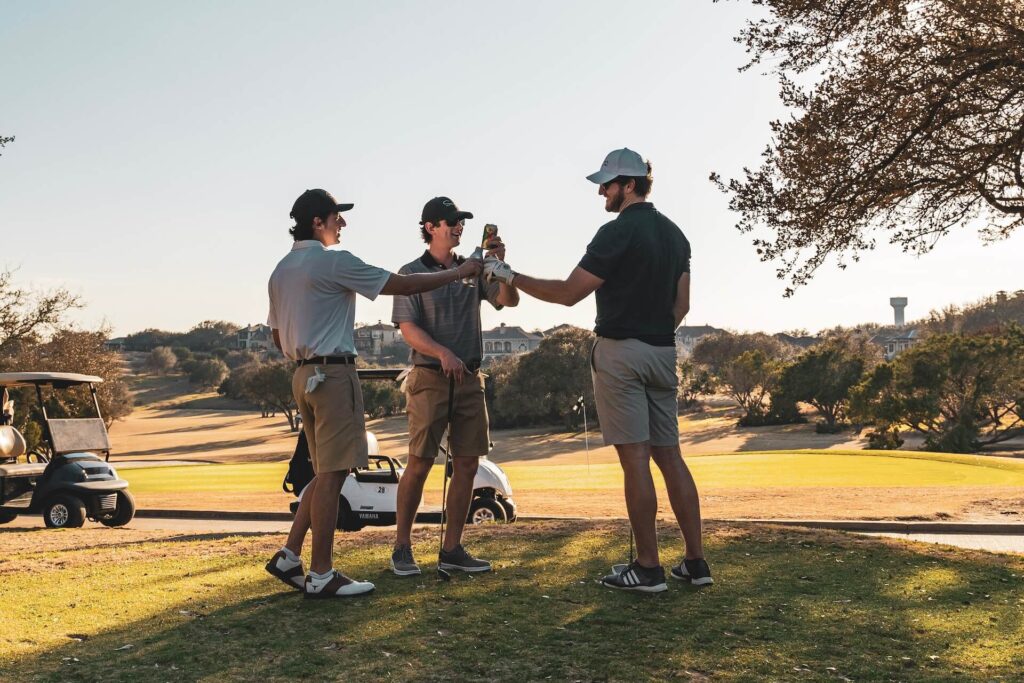 Three guys celebrate with beverages on the golf course.