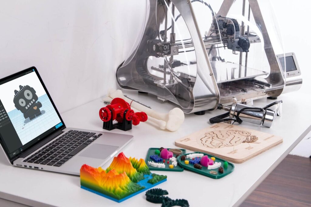 A 3D printer sits next to a laptop with previously created products. 