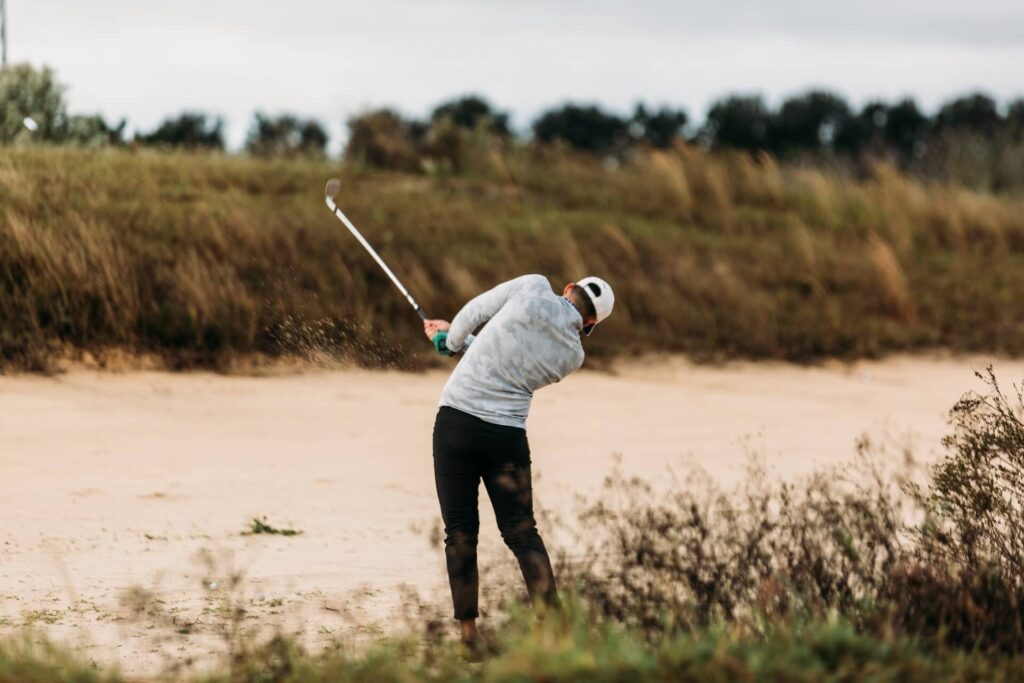 Golfer hitting the ball out of a bunker with deep rough all around