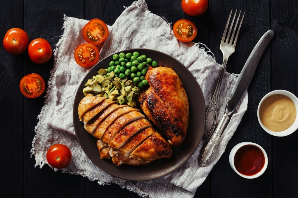 A plate of baked chicken, avocado and peas.