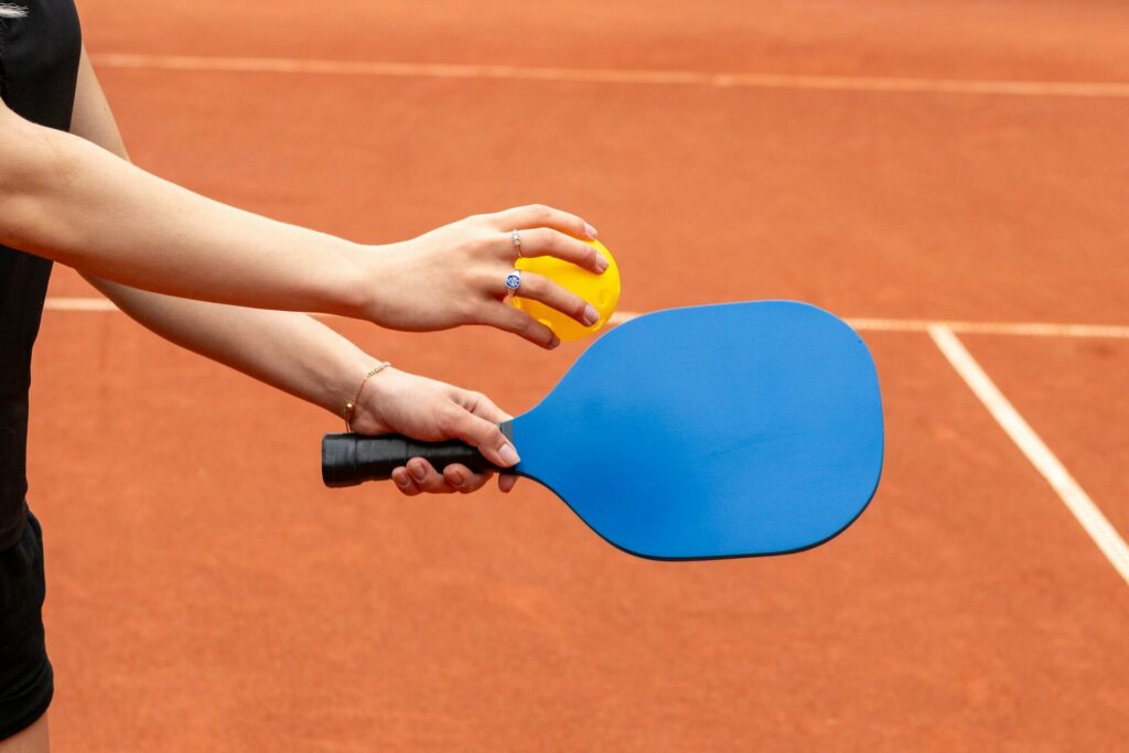 Person holding a pickleball paddle and ball on the court.