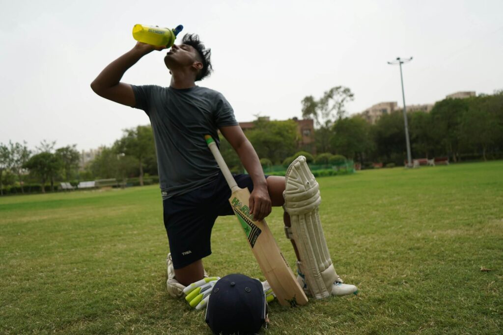 Man kneeling with cricket equipment and drinking water